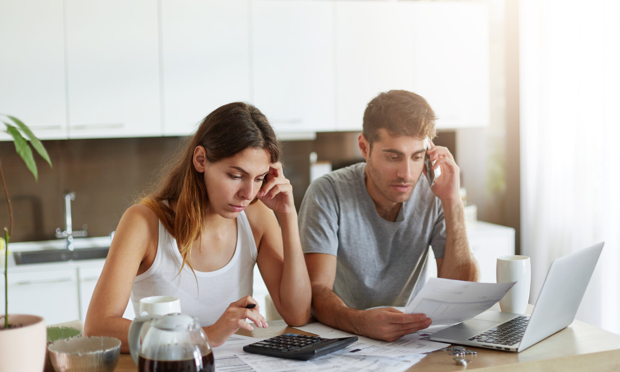 Indoor Shot Of Serious Couple Of Business Workers Being Busy At Home While Reading Attentively Documents, Making Financial Report And Calculating Annual Figures, Making Arrangements Over Mobile Phone - RW Office