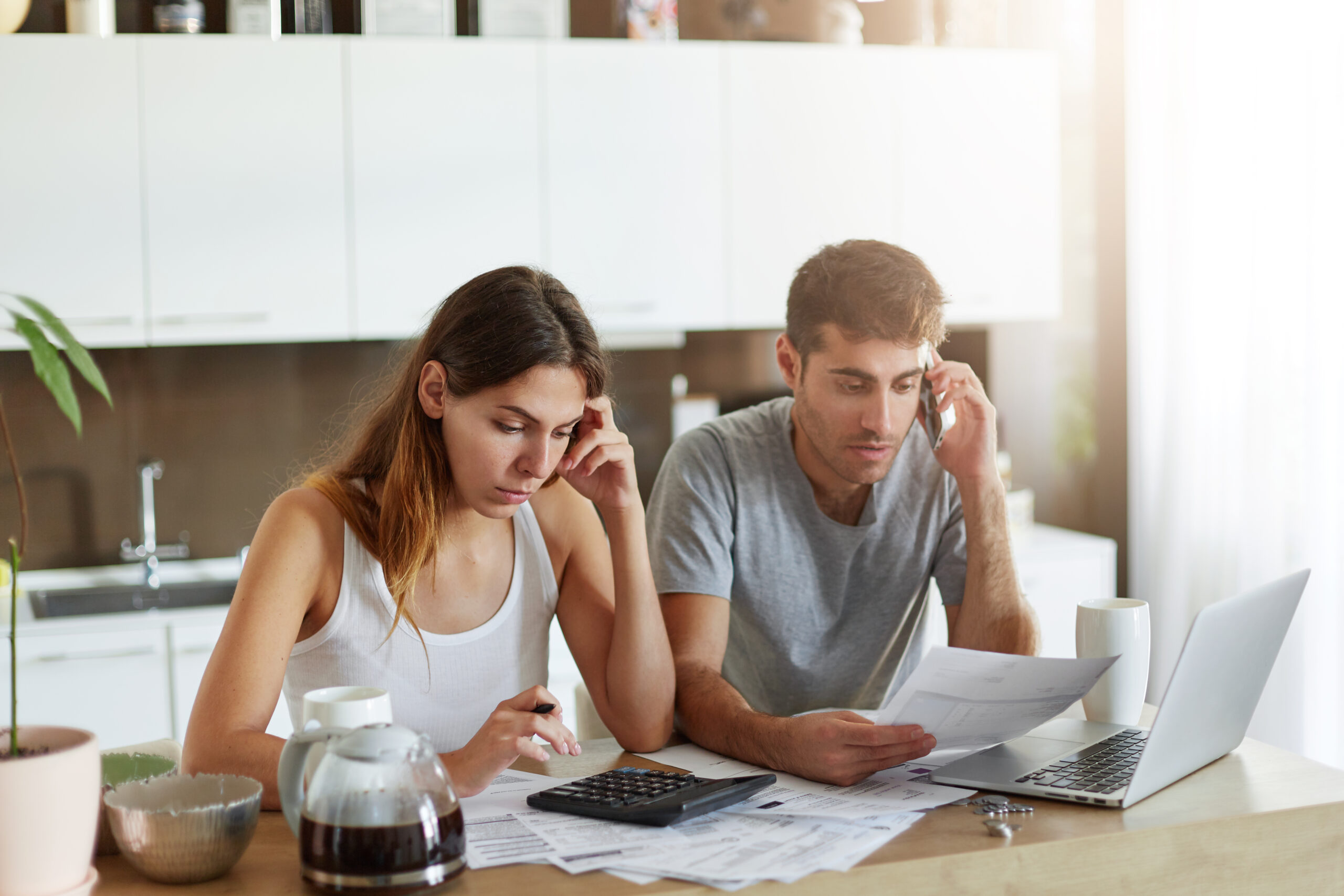 Indoor Shot Of Serious Couple Of Business Workers Being Busy At Home While Reading Attentively Documents, Making Financial Report And Calculating Annual Figures, Making Arrangements Over Mobile Phone - RW Office